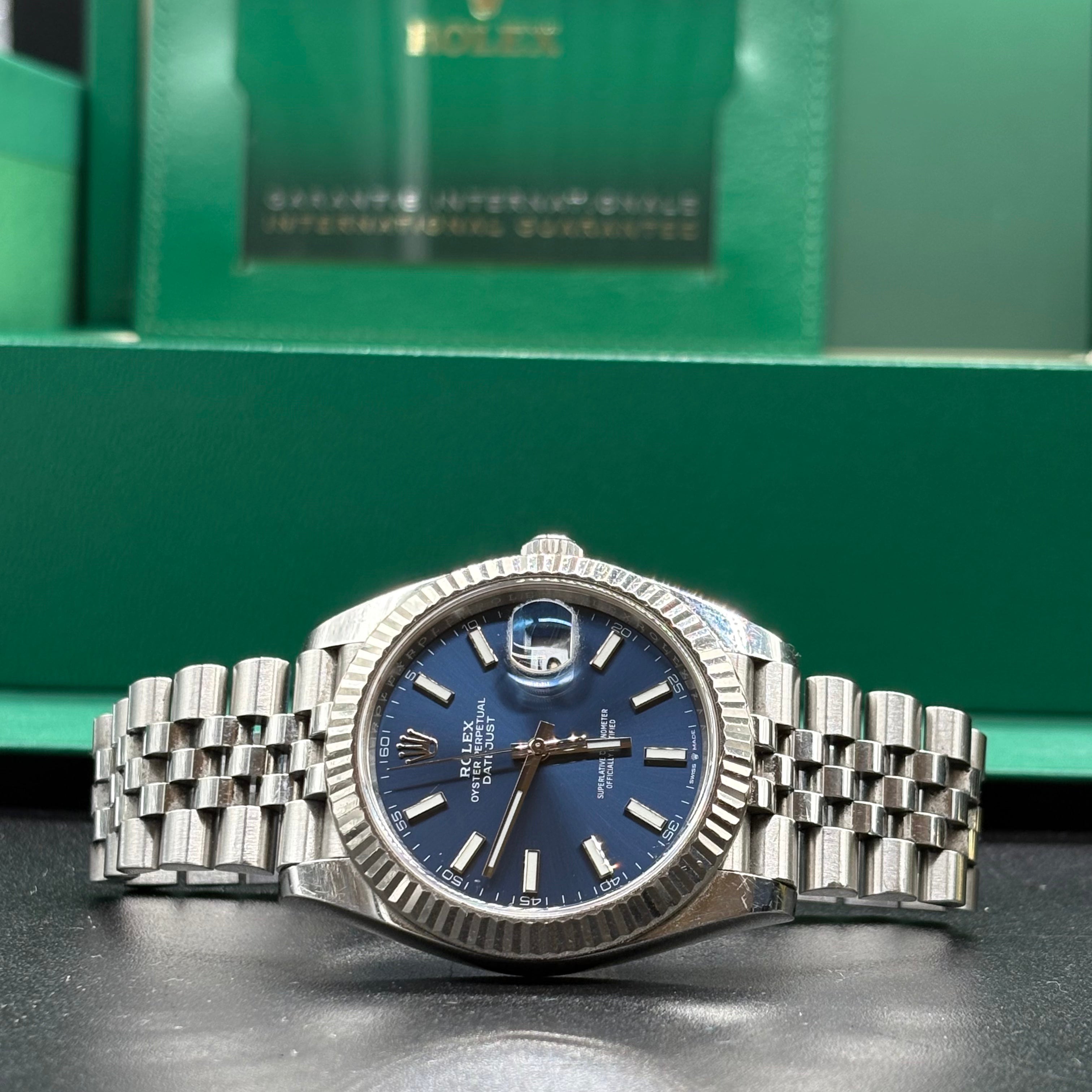 Rolex Datejust 41mm blue dial side on view of the fluted bezel with International Guarantee wallet behind
