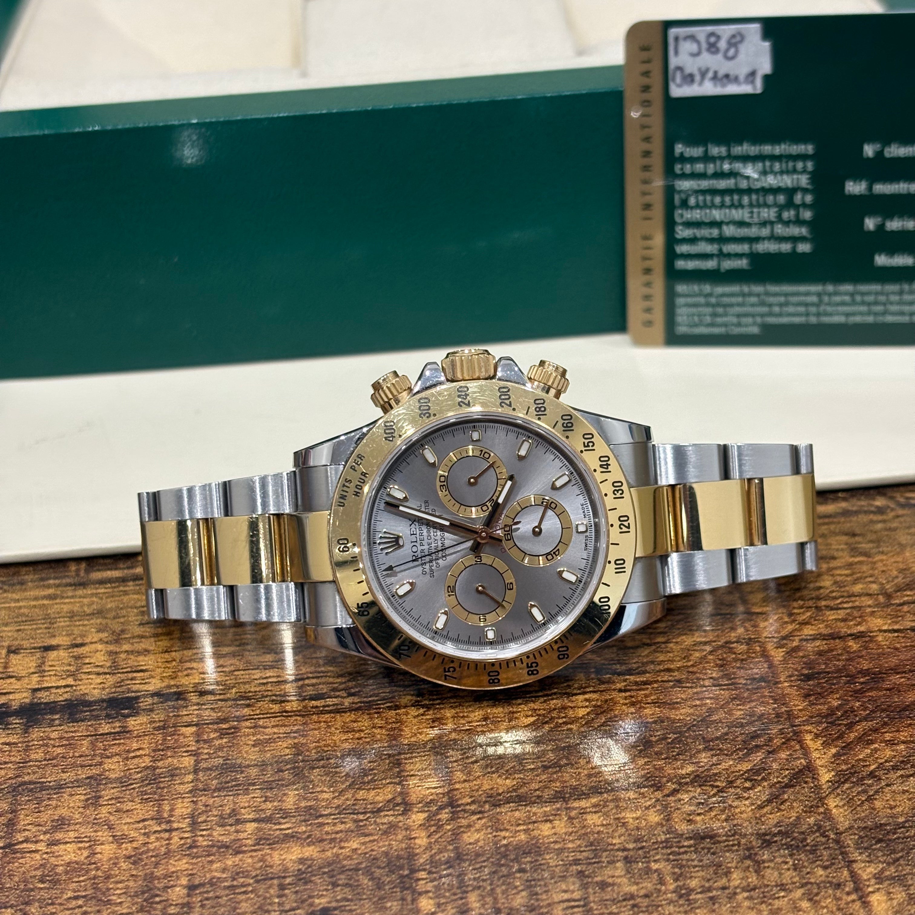 Rolex Cosmograph Daytona two tone silver dial wide view on a wooden surface with its guarantee card