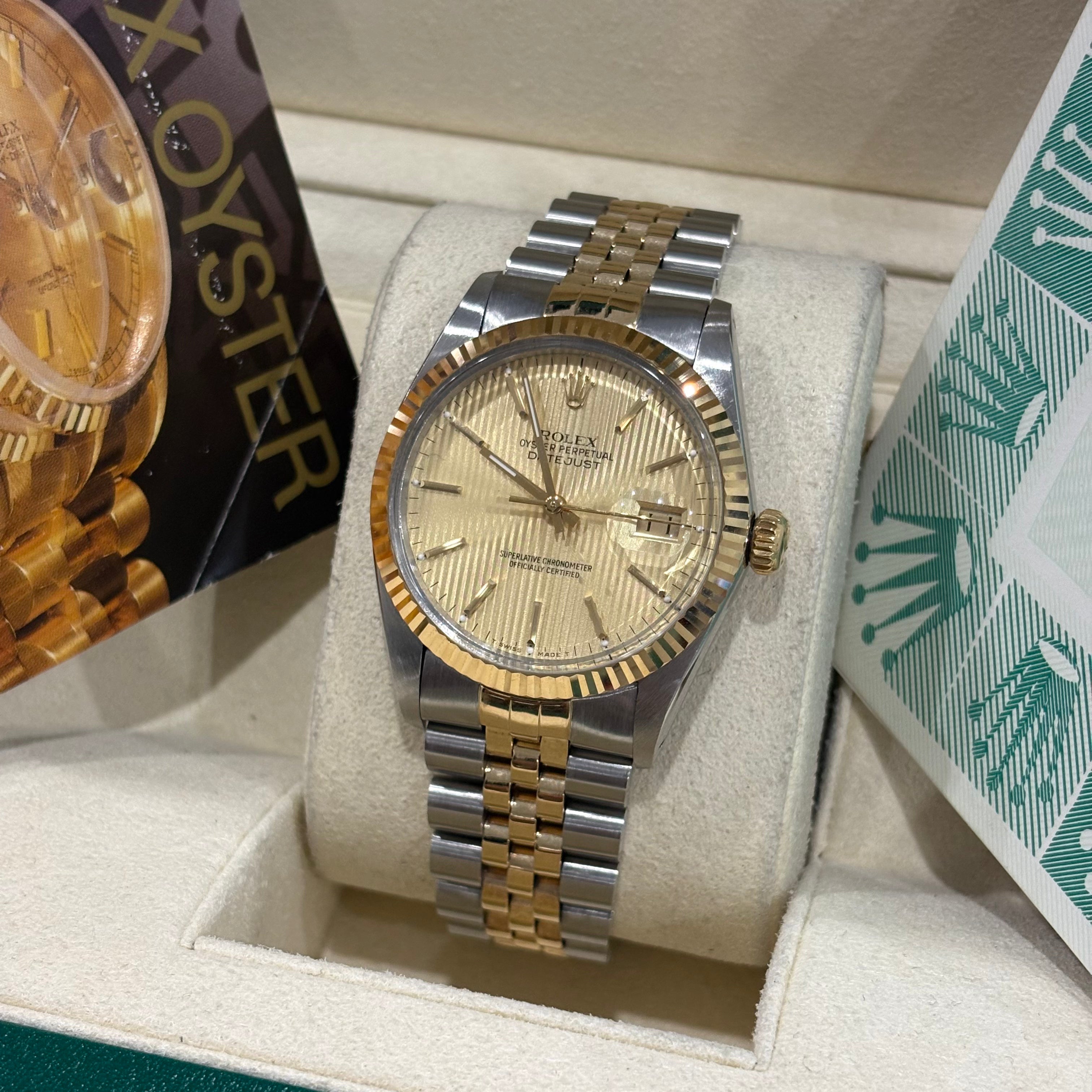 Rolex Datejust 36 two tone tapestry dial front view on its cushion beside the Rolex Oyster booklet