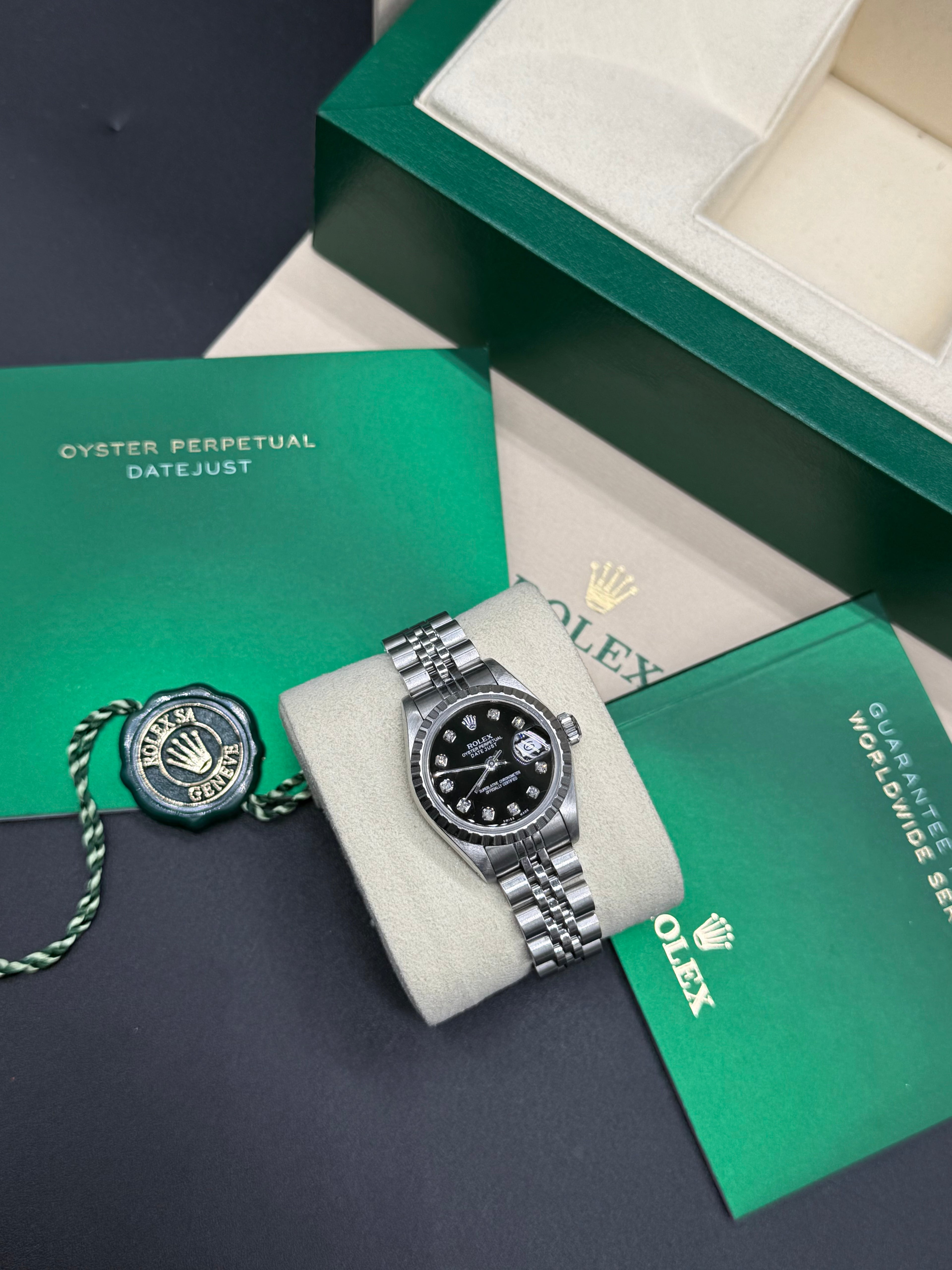 Rolex watch on a display stand with green box and papers in the background